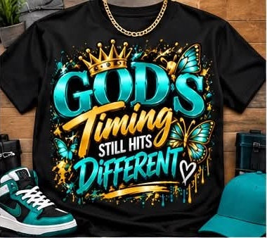Black God's Timing Still Hits Different graphic T-shirt with teal, gold, and white lettering, teal butterflies, a gold-toned crown, and hearts; styled with accessories.