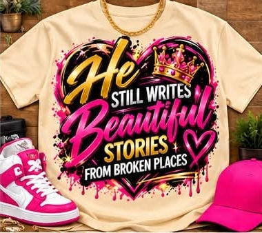 Cream-colored He Still Writes Beautiful Stories From Broken Places graphic T-shirt with pink, gold, and white lettering, heart artwork, and a crown; styled with accessories.